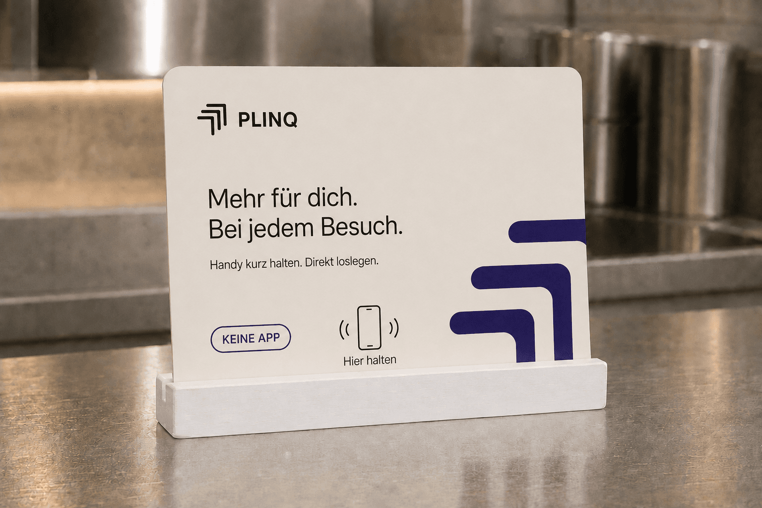 Aufsteller auf einem Edelstahltresen: PLINQ-Logo, die Zeile „Mehr für dich. Bei jedem Besuch.“ und der Hinweis „Hier halten“.